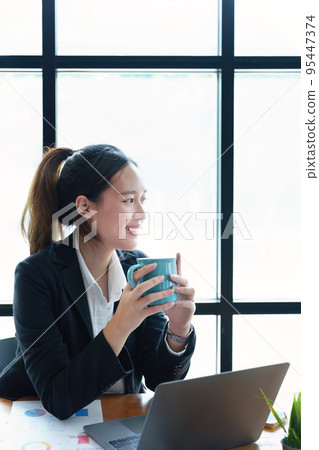 Portrait of a young woman drinking coffee while using a computer. 95447374