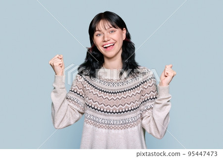 Happy woman showing clenching fists, raising hands up on grey background 95447473