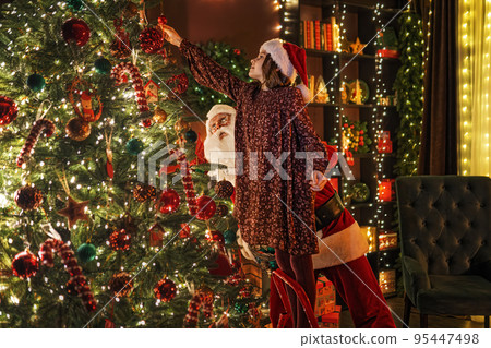 Little girl with Santa Claus together decorating Christmas tree with toys. New Year concept. Little girl with Santa Claus together decorating Christmas tree with toys. New Year concept. 95447498