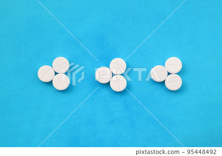 Several white tablets lie on a bright blue background in the form of three triangular arrows. Background image on medicine and pharmaceutical topics 95448492