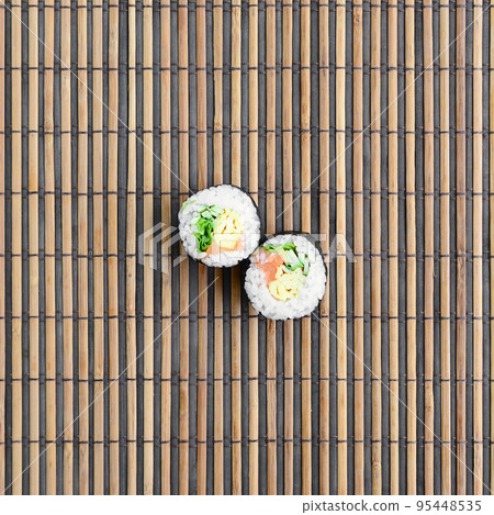 Sushi rolls lies on a bamboo straw serwing mat. Traditional Asian food. Top view. Flat lay minimalism shot with copy space Sushi rolls lies on a bamboo straw serwing mat. Traditional Asian food. Top view. Flat lay minimalism shot with copy space 95448535