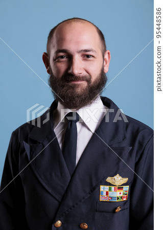 Smiling airplane pilot wearing uniform medium close up portrait, plane captain looking at camera. Middle age aviator with civil badge on professional suit, aircrew member Smiling airplane pilot wearing uniform medium close up portrait, plane captain looking at camera. Middle age aviator with civil badge on professional suit, aircrew member 95448586