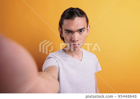 Angry man talking on video call, taking selfie on smartphone, looking at front camera first person view. Asian teeanger holding mobile phone, with annoyed facial expression pov Angry man talking on video call, taking selfie on smartphone, looking at front camera first person view. Asian teeanger holding mobile phone, with annoyed facial expression pov 95448648