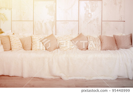 Many pillows lie on the couch, which is covered with a large plush veil against the background of a marble wall 95448999