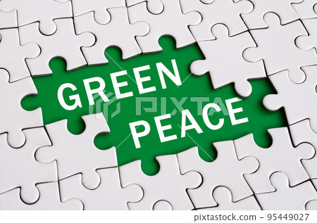 White jigsaw puzzle in assembled state with missing elements forming a green space with white inscription. Green peace 95449027
