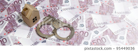 Scam with real estate. Cheating when buying or renting a house. Punishment for deception. A toy house with handcuffs on a many 500 purple euro banknotes 95449036