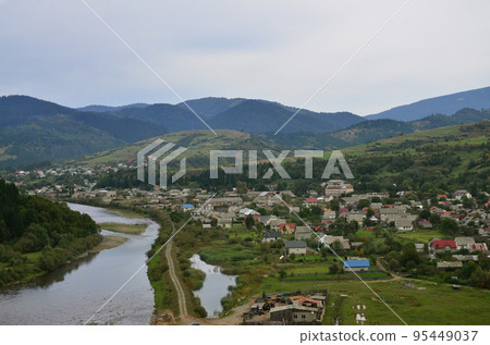 A beautiful view of the village of Mezhgorye, Carpathian region. A lot of residential buildings surrounded by high forest mountains and long river 95449037