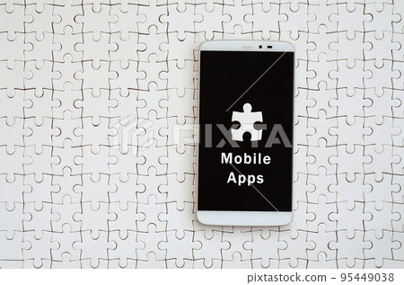 A modern big smartphone with a touch screen lies on a white jigsaw puzzle in an assembled state with inscription. Mobile apps A modern big smartphone with a touch screen lies on a white jigsaw puzzle in an assembled state with inscription. Mobile apps 95449038