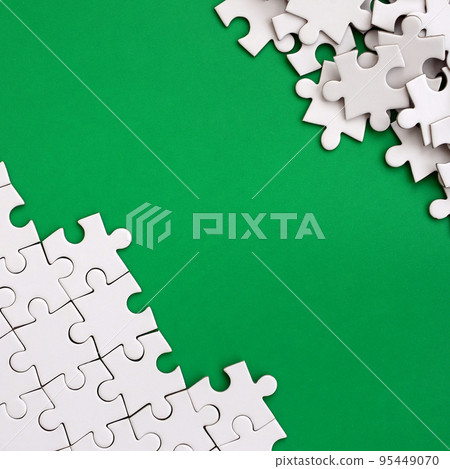 Fragment of a folded white jigsaw puzzle and a pile of uncombed puzzle elements against the background of a green surface. Texture photo with space for text Fragment of a folded white jigsaw puzzle and a pile of uncombed puzzle elements against the background of a green surface. Texture photo with space for text 95449070