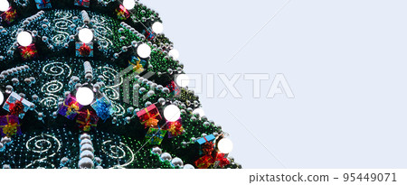 A fragment of a huge Christmas tree with many ornaments, gift boxes and luminous lamps. Photo of a decorated Christmas tree close-up with copy space A fragment of a huge Christmas tree with many ornaments, gift boxes and luminous lamps. Photo of a decorated Christmas tree close-up with copy space 95449071