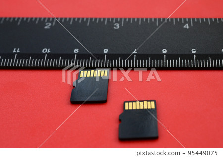 Two small micro SD memory cards lie on a red background next to a black ruler. A small and compact data and information store 95449075