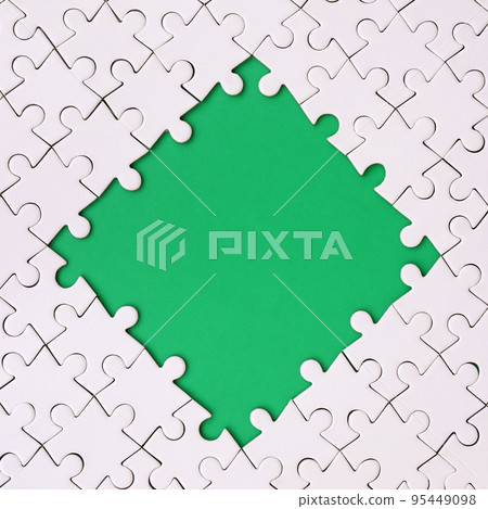 Framing in the form of a rhombus, made of a white jigsaw puzzle around the green space 95449098