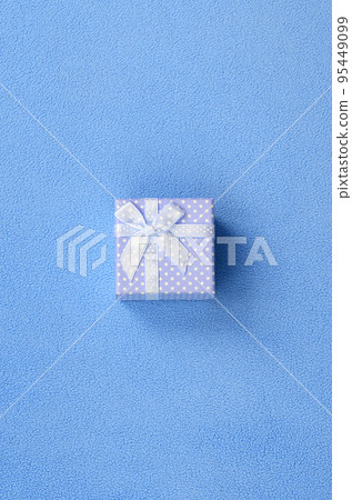 A small gift box in blue with a small bow lies on a blanket of soft and furry light blue fleece fabric. Packing for a gift to your lovely girlfriend 95449099