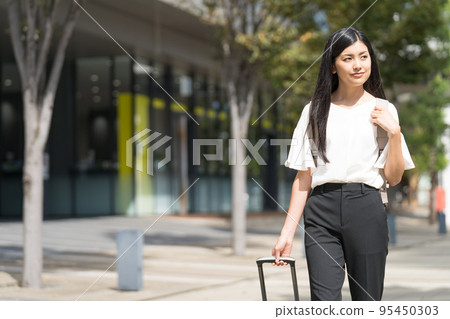 A businesswoman walking with a backpack and a suitcase 95450303