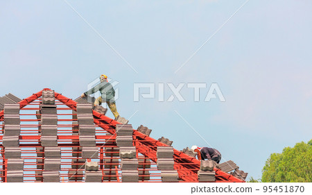 Construction roofer installing roof tiles at house building site 95451870