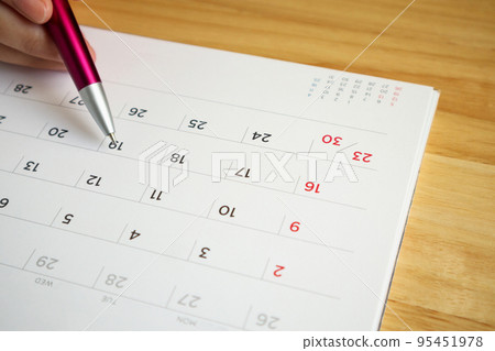 calendar page with female hand holding pen on desk table 95451978