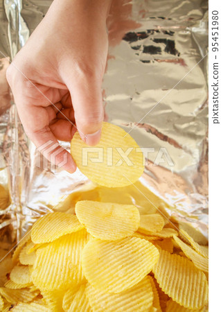 Hand hold potato chips inside snack foil bag 95451980