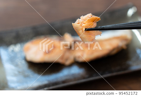 He is picking up grilled salmon from Hokkaido with chopsticks. 95452172