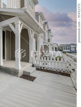 Vertical Puffy clouds at sunset Front entrance of a light brown townhouse with white picket fenc Vertical Puffy clouds at sunset Front entrance of a light brown townhouse with white picket fenc 95452372