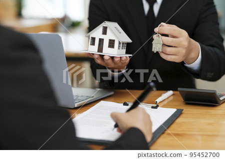 Real estate agent giving house keys to client after signing home loan contract. 95452700