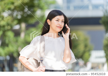 A business woman carrying a backpack and making a phone call with a smartphone A business woman carrying a backpack and making a phone call with a smartphone 95452810