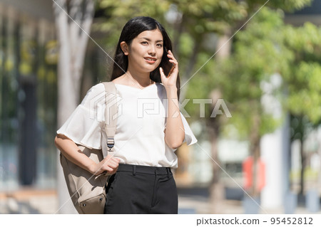 A business woman carrying a backpack and making a phone call with a smartphone A business woman carrying a backpack and making a phone call with a smartphone 95452812