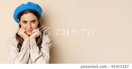 Close up portrait of feminine young woman in trendy french hat, posing cute and romantic, making silly coquettish face and tender smile, beige background Close up portrait of feminine young woman in trendy french hat, posing cute and romantic, making silly coquettish face and tender smile, beige background 95453387