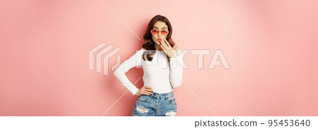 Coquettish and stylish brunette girl, laughing and smiling, wearing sunglasses, wearing white blouse and jeans, pink background Coquettish and stylish brunette girl, laughing and smiling, wearing sunglasses, wearing white blouse and jeans, pink background 95453640