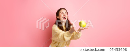 Happy cute girl catches an apple and laughs, time for healthy lunch filled with fruits, stands against pink background 95453698
