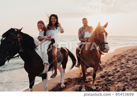 The family spends time with their children while riding horses together on a sandy beach. Selective focus The family spends time with their children while riding horses together on a sandy beach. Selective focus 95453699