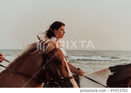 Woman in summer clothes enjoys riding a horse on a beautiful sandy beach at sunset. Selective focus Woman in summer clothes enjoys riding a horse on a beautiful sandy beach at sunset. Selective focus 95453701