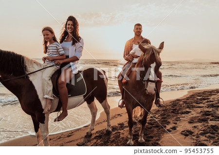 The family spends time with their children while riding horses together on a sandy beach. Selective focus The family spends time with their children while riding horses together on a sandy beach. Selective focus 95453755