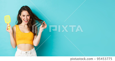 Happy attractive woman showing her brush without hair strand and touching healthy long hairstyle with pleased face, smiling delighted with shampoo result, blue background 95453775