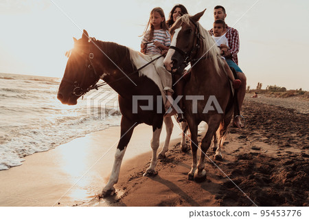 The family spends time with their children while riding horses together on a sandy beach. Selective focus The family spends time with their children while riding horses together on a sandy beach. Selective focus 95453776