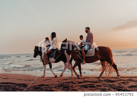 The family spends time with their children while riding horses together on a sandy beach. Selective focus The family spends time with their children while riding horses together on a sandy beach. Selective focus 95453791