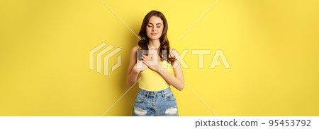 Young woman in tank top, holding hands on heart with care and tenderness, smiling at camera, looking grateful, thankful, standing over yellow background Young woman in tank top, holding hands on heart with care and tenderness, smiling at camera, looking grateful, thankful, standing over yellow background 95453792