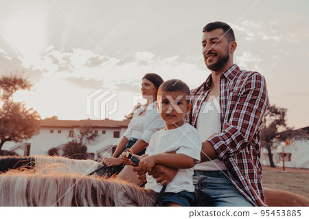 The family spends time with their children while riding horses together on a sandy beach. Selective focus  95453885
