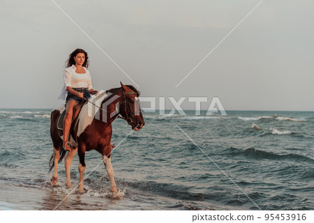 Woman in summer clothes enjoys riding a horse on a beautiful sandy beach at sunset. Selective focus  95453916