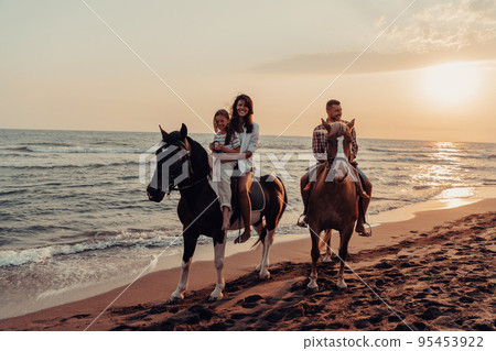 The family spends time with their children while riding horses together on a sandy beach. Selective focus The family spends time with their children while riding horses together on a sandy beach. Selective focus 95453922