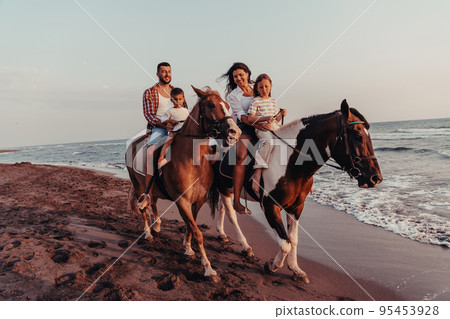 The family spends time with their children while riding horses together on a sandy beach. Selective focus  95453928