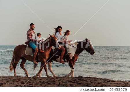 The family spends time with their children while riding horses together on a sandy beach. Selective focus The family spends time with their children while riding horses together on a sandy beach. Selective focus 95453979
