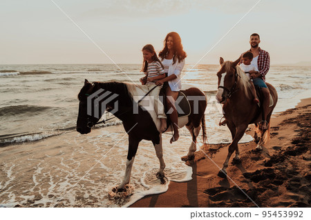 The family spends time with their children while riding horses together on a sandy beach. Selective focus  95453992