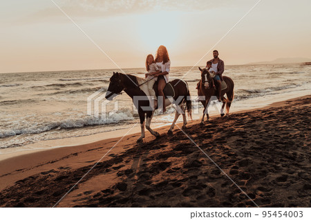 The family spends time with their children while riding horses together on a sandy beach. Selective focus The family spends time with their children while riding horses together on a sandy beach. Selective focus 95454003
