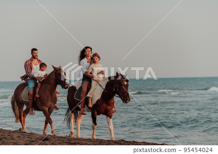 The family spends time with their children while riding horses together on a sandy beach. Selective focus The family spends time with their children while riding horses together on a sandy beach. Selective focus 95454024