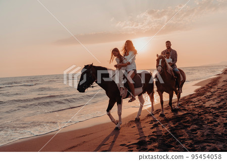 The family spends time with their children while riding horses together on a sandy beach. Selective focus  95454058