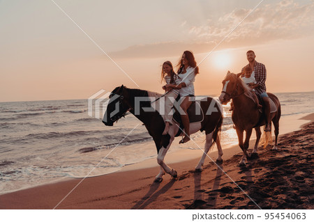 The family spends time with their children while riding horses together on a sandy beach. Selective focus The family spends time with their children while riding horses together on a sandy beach. Selective focus 95454063