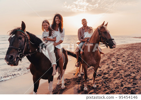 The family spends time with their children while riding horses together on a sandy beach. Selective focus The family spends time with their children while riding horses together on a sandy beach. Selective focus 95454146