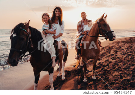 The family spends time with their children while riding horses together on a sandy beach. Selective focus The family spends time with their children while riding horses together on a sandy beach. Selective focus 95454147