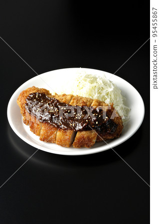 Pork cutlet and shredded cabbage with miso-based sauce photographed against a black background 95455867