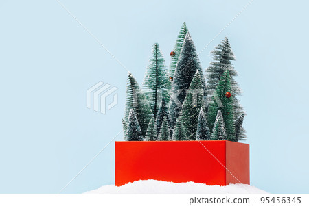 red gift box with many small Christmas trees in snow pile on blue background. Variety of choice. Seasonal ornaments shopping and sale concept. Greeting card. copy space 95456345